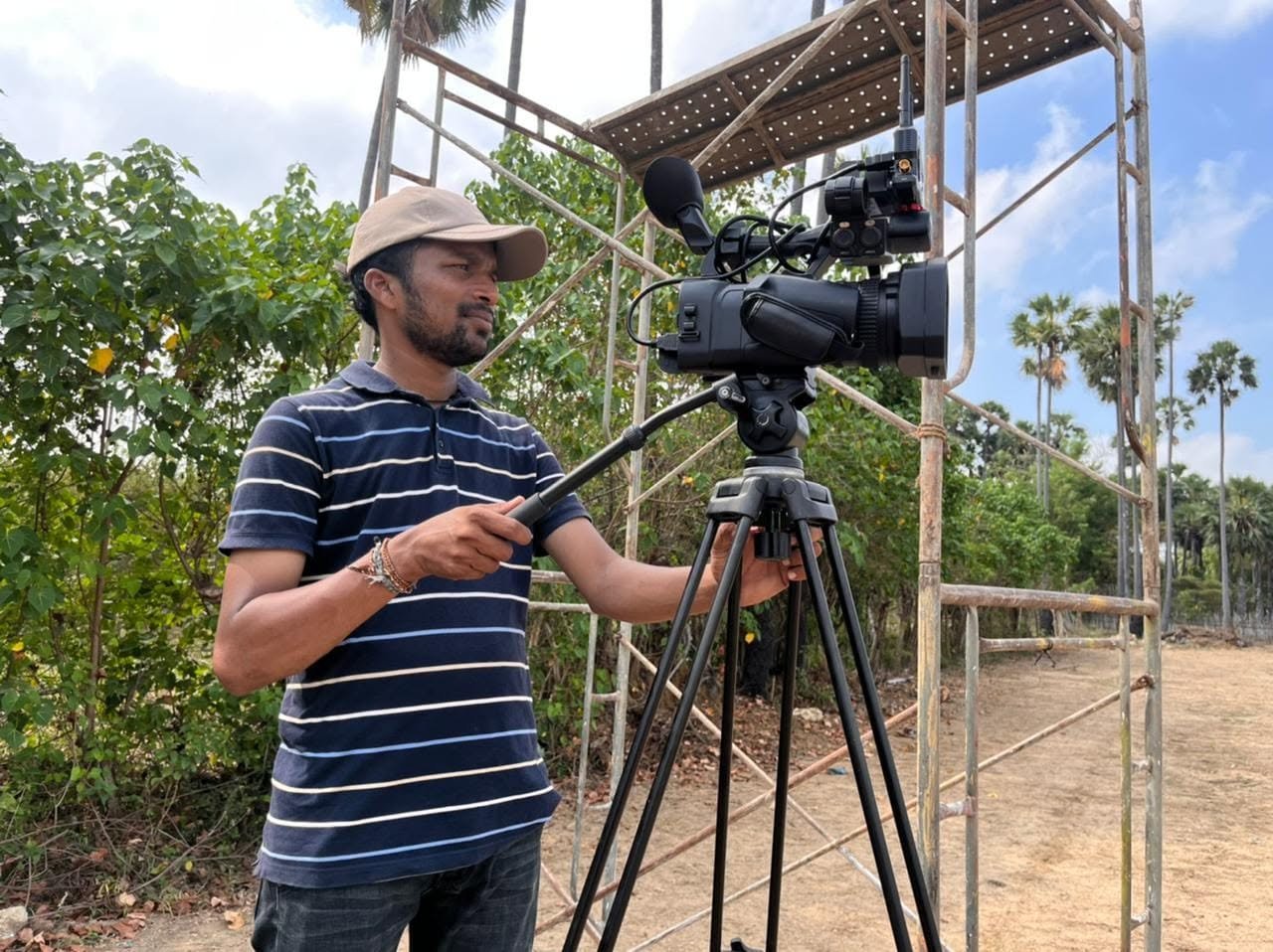 Camera operator setting up a camcorder on a tripod beside scaffolding