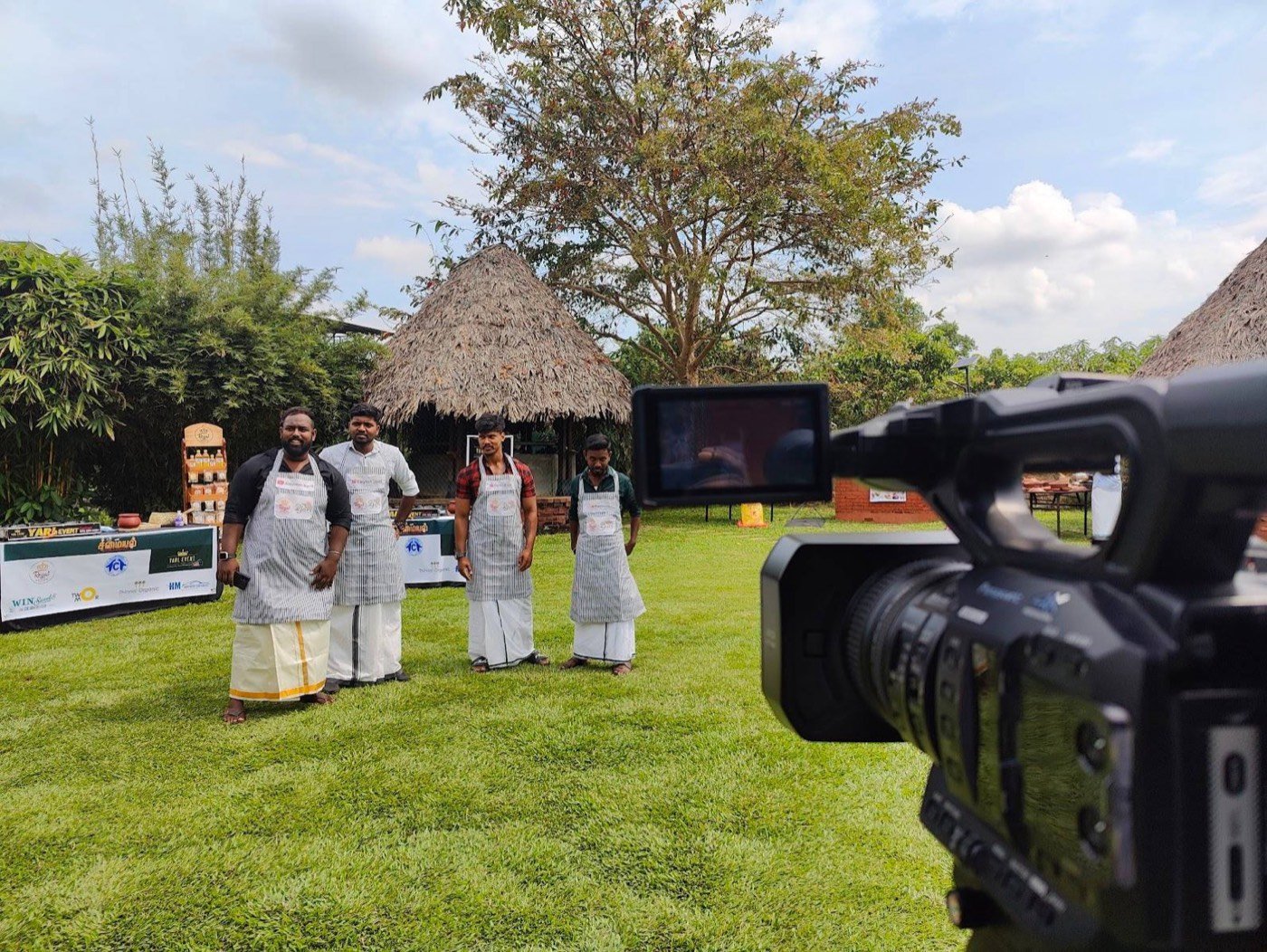 Contestants in aprons lined up for a cooking show, filmed outdoors